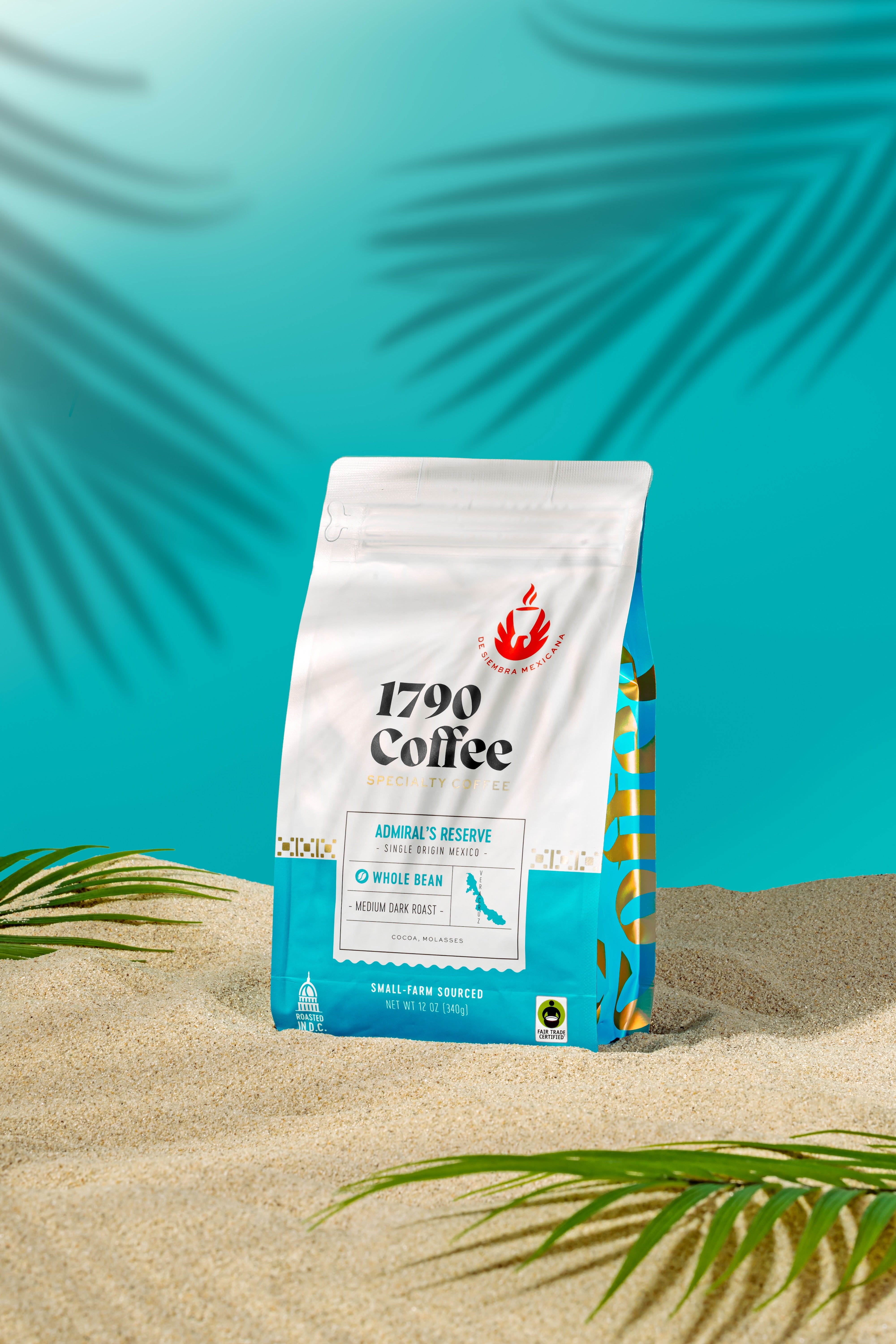 Bag of 1790 Coffee Admiral's Reserve on sand with palm leaves against a blue background